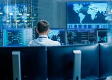 Back View in the System Control Center Operator Working. Multiple Screens Showing Technical Data.